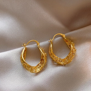 Gros plan détaillé de boucles d'oreilles créoles torsadées dorées sur tissu satiné.