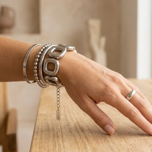Dettaglio di bracciali e anello in acciaio inossidabile argento su mano con sfondo legno.
