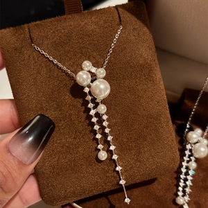 Elegant long zircon tassel and white pearl pendant necklace close-up on brown velvet.