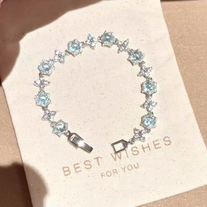 Elegant silver-tone link bracelet with light blue and clear zircons on a cream gift pouch