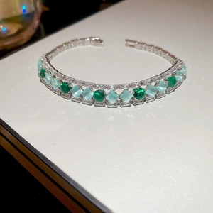 Close-up of luxury bracelet featuring emerald green and light blue zircons on white