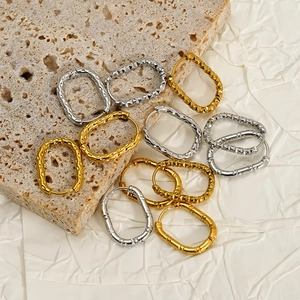 Close-up of textured oval hoop earrings in gold and silver finishes on a stone base