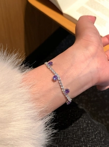 Detailaufnahme eines eleganten Silberarmbands mit runden lila Zirkonia-Steinen am Handgelenk.