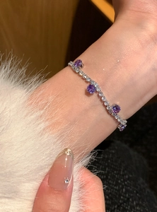 Nahaufnahme eines silbernen Tennisarmbands mit lila Zirkonsteinen am weiblichen Handgelenk.