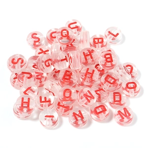 Close-up of clear acrylic alphabet beads with red letters and pre-drilled holes for DIY jewelry