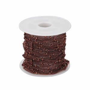 Detailed macro view of 1.5mm vintage copper beaded flat chain on a white plastic spool