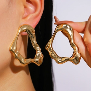 Irregular wavy gold hoop earrings with polished finish shown on ear and held in hand
