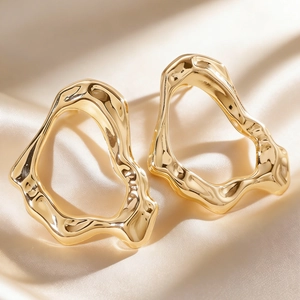 Close-up of golden irregular liquid metal earrings on soft champagne silk background.