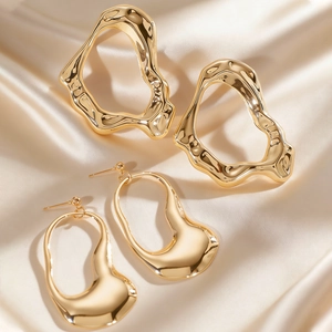 Close-up of gold irregular liquid metal geometric earrings on champagne silk background