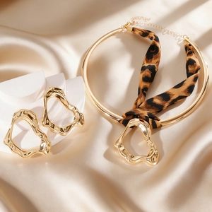 Close-up of golden irregular liquid metal earrings and leopard print ribbon choker set.
