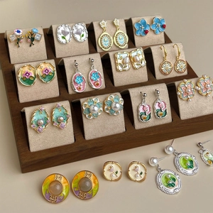 Macro detail of various enamel floral and pearl earrings on a professional display stand.