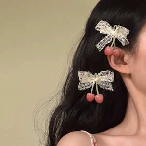 Detail of two sweet lace bow hair clips with pink cherry pendants on wavy black hair.
