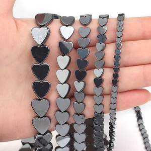 Five sizes of heart-shaped hematite loose beads displayed on hand for scale