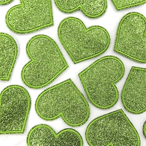 Macro detail of grass green glitter heart patches with shiny sequins and embroidery