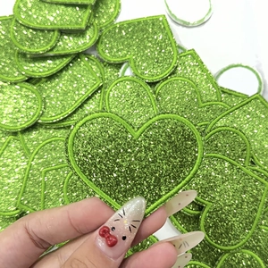 Macro detail of heart embroidery patch with green glitter texture and fine border stitching