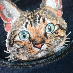 Macro shot of tabby cat embroidery with blue eyes on dark blue denim fabric