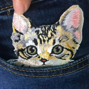 Cat head embroidery patch with detailed brown and black stripes shown on denim pocket
