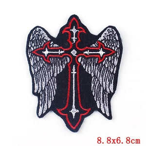 Macro detail of gothic cross embroidery patch with silver wings and red border