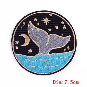 Detail of a 7.5cm round embroidered patch with a whale tail and starry night sky design