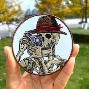 Round punk skull photographer embroidered patch on a denim jacket background
