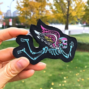 Détail d'un écusson brodé montrant un squelette bleu avec des ailes en plumes roses