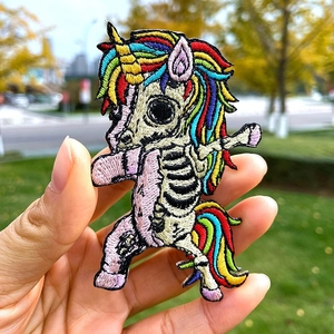 Écusson brodé de squelette de licorne arc-en-ciel tenu à la main sur un fond extérieur naturel