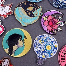 Close-up of artistic embroidered patches with whale, floral moon and No-Face designs