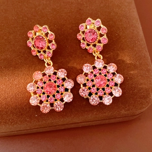 Detalle macro de pendientes vintage dorados con diseño de flores de cristal rosa