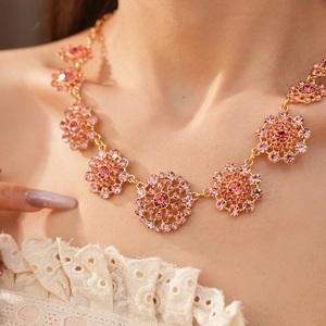 Primer plano de un collar vintage dorado con cristales rosas y diseños circulares