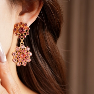 Primer plano de elegantes pendientes vintage dorados con pedrería rosa lucidos por una modelo