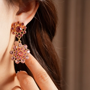 Detalle de cerca de pendientes vintage dorados con diseño floral de pedrería rosa