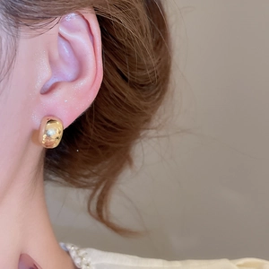 Detail shot of a chunky gold hoop earring on a woman's ear, showing shiny mirror finish.