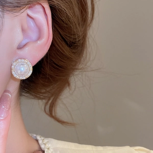 Close-up of a elegant white pearl stud earring worn on an ear, luxury gold finish detail