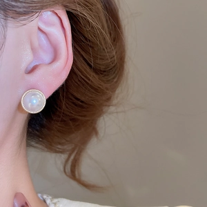 Detail of a cat's eye stone stud earring worn on an ear with gold textured rim