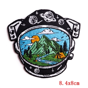 Detail of embroidered astronaut helmet patch showing mountain landscape and cosmic planets