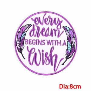 Macro detail of 8cm circular embroidery patch with motivational dream and wish slogan