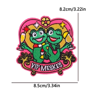 Detailed embroidery patch showing two green frogs with wine glasses on a pink heart base