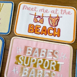 Macro view of embroidered patches with Meet me at the beach and Babes support babes text