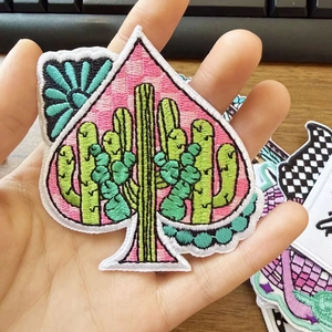 Detail of embroidered spade patch with cactus and pink checkerboard pattern held by hand