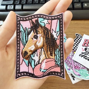 Detailed close-up of a horse embroidery patch held by hand over a wooden desk