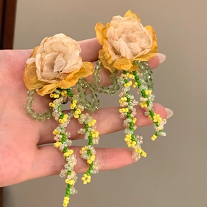 Primo piano dettagliato di orecchini con nappe a fiori gialli e fili di perline verde-giallo