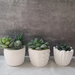 Three artificial succulents in white patterned ceramic pots on a linen tablecloth