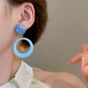 Detailed close-up view of retro style blue marble stud and large hoop earrings on model ear