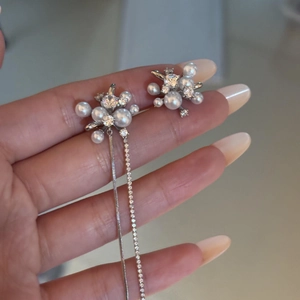Primo piano di orecchini asimmetrici con perle bianche e zirconi brillanti incastonati.