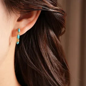 Vintage gold-plated C-shaped earrings with turquoise stones and zircons worn on ear