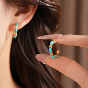 Detail of a vintage gold-plated C-shaped hoop earring with turquoise stones and zircons.