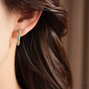 Detail view of vintage gold-plated C-shaped earring with turquoise stones on a model.