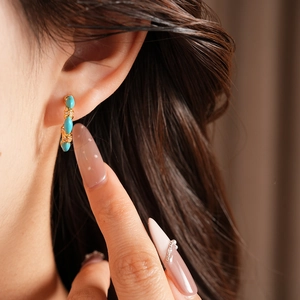 Close-up of vintage C-shaped gold-plated earring with turquoise stones and zircon details