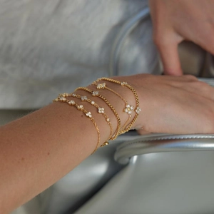 Close-up of layered gold stainless steel bracelets with white zircon clover charms.