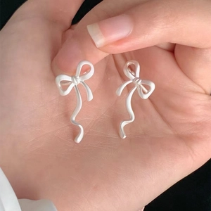 Detaillierte Nahaufnahme von minimalistischen weißen Schleifen-Clip-Ohrringen auf einer Hand